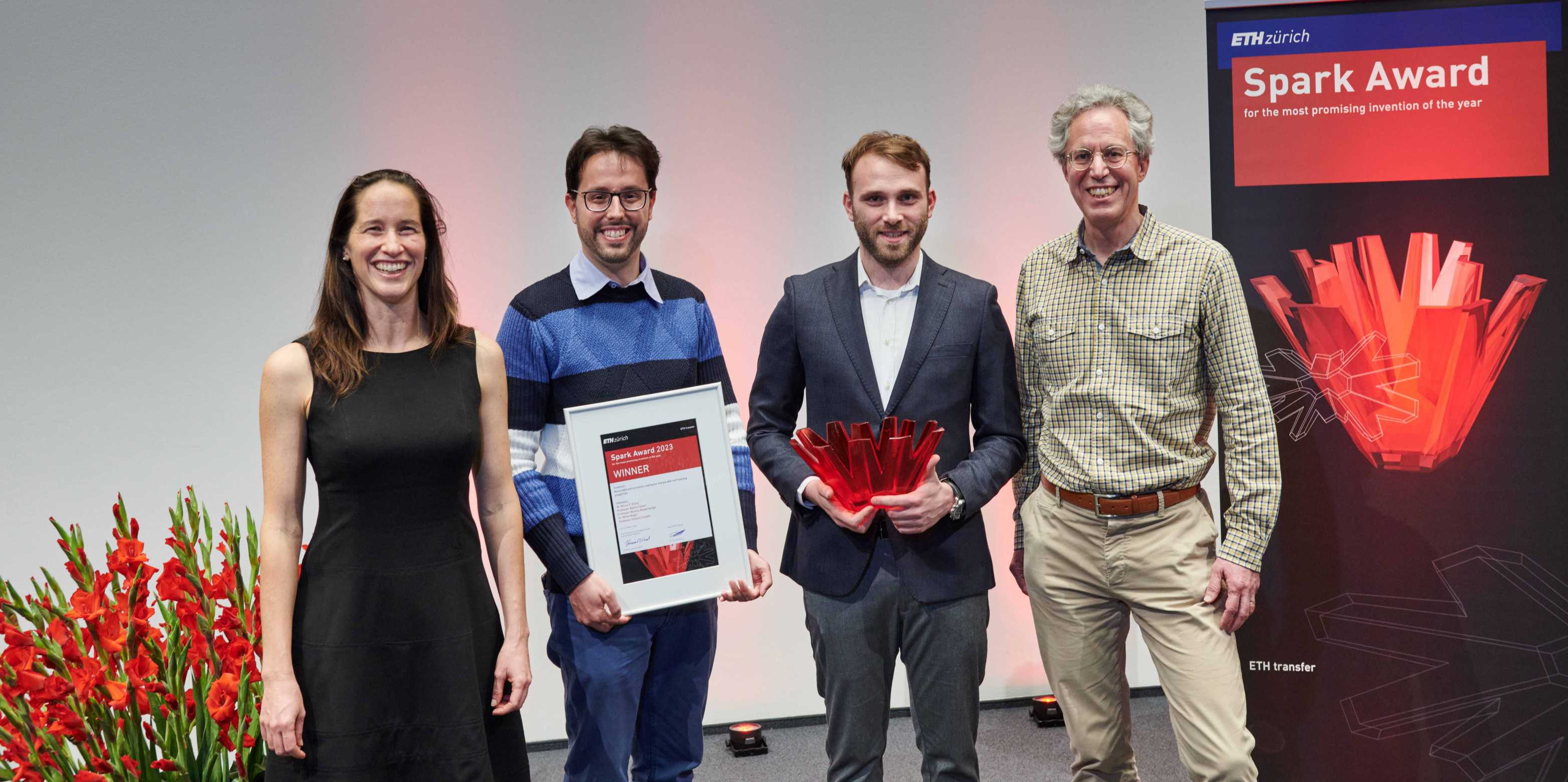 The three winners of the Spark Award 2023 stand to the right of Vanessa Wood. They hold the award and the prize in their hands.